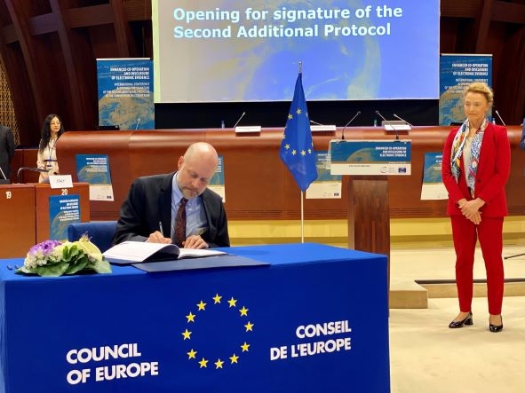 Man sitting at table titled "Council of Europe" and signing paper