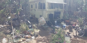 Photo of small camper surrounded by garbage in the woods