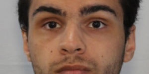 Photo of a man with dark hair and a dark shirt against a white wall.