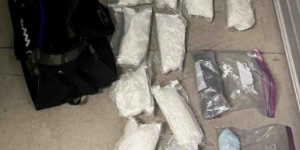 Photo of multiple bags of white and blue drugs with a black bag to the left of the substances. 