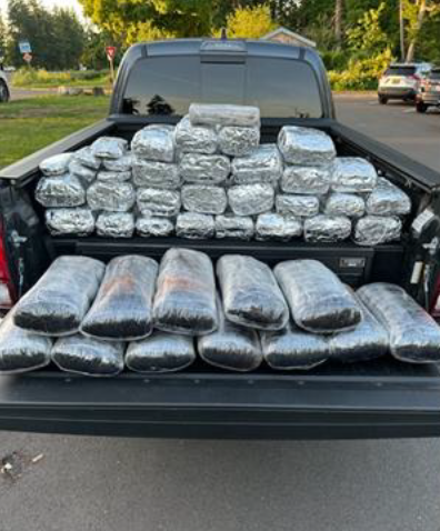 Law enforcement image. Black flatbed truck. Truck bed is filled with drugs wrapped in plastic and shaped into bricks. The truck is in a parking lot.