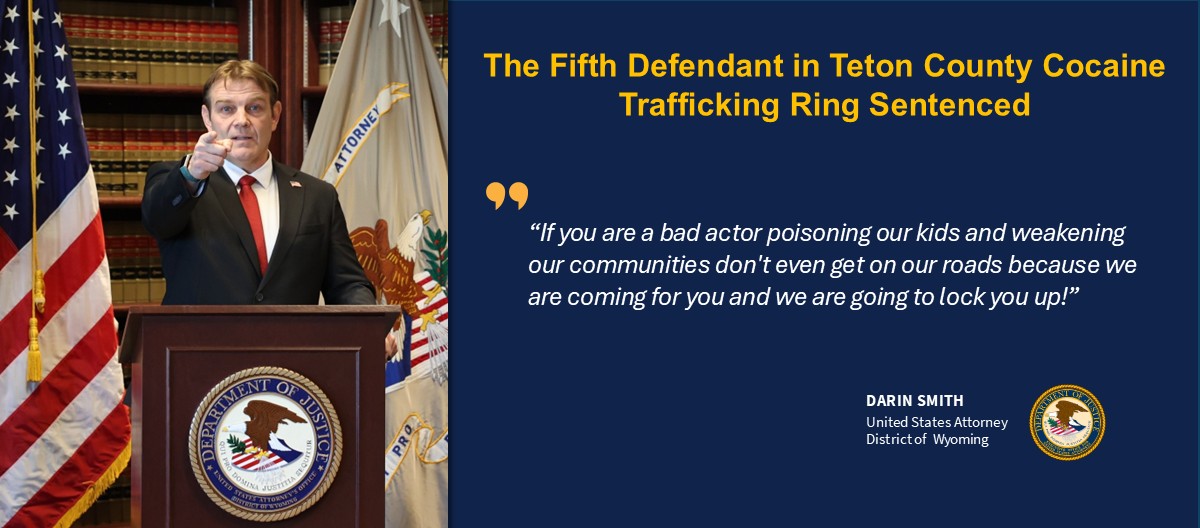 U.S. Attorney Darin Smith speaks at a press conference. He is point towards the crowd as he stands behind a podium flanked by the American and U.S. Attorney flags.