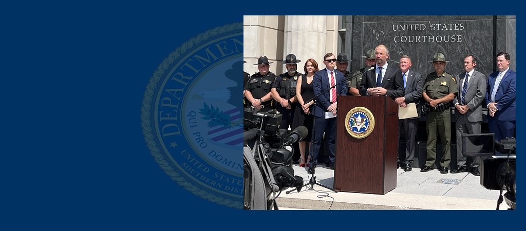 Photo of U.S. Attorney Moore Capito at the podium during a press conference outside the Robert C. Byrd U.S. Courthouse in Charleston, W.Va., with law enforcement and other officials in a row standing behind him.