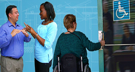 image showing two people using sign language and a woman using a wheelchair opening a door image showing two people using sign language and a woman using a wheelchair opening a door