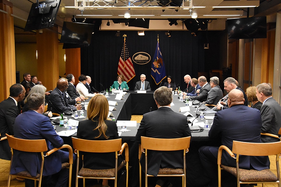 Officials of law enforcement sit in a round table formation. To the left in green is Deputy Attorney General Lisa O. Monaco, in the middle we see Attorney General Merrick B. Garland, and to the right of the Attorney General is Associate Attorney General Vanita Gupta.