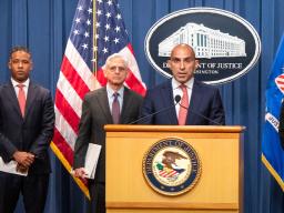 Assistant Director Luis Quesada of the FBI’s Criminal Investigative Division speaks at the podium with a Department of Justice seal. Behind him are Assistant Attorney General Kenneth A. Polite, Jr. of the Justice Department’s Criminal Division and Attorney General Merrick B. Garland.
