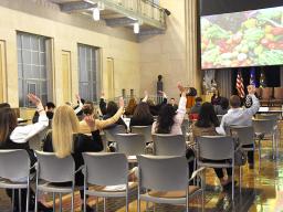Individuals from many federal departments and organizations participate in the Reentry Simulation, raising their hands in response to a question.