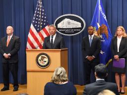 Deputy Secretary John K. Tien (D.H.S.) speaks at a podium bearing the Department of Justice Seal.