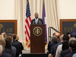 Dean Troy McKenzie of NYU’s School of Law speaks to an audience of officials and attorneys at a podium bearing the New York University seal.