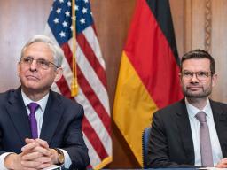 Attorney General Merrick B. Garland and the German Minister of Justice Dr. Marco Buschmann sit in front of the flag of the United States of America and the flag of Germany, respectively