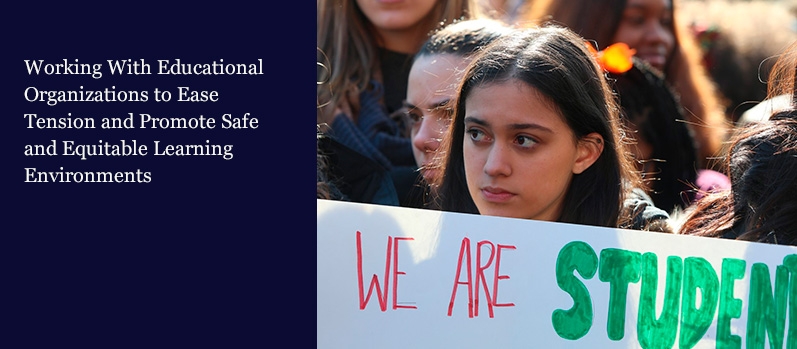 Closeup of a young female student in a crowd holding a sign saying, “We are students.” 