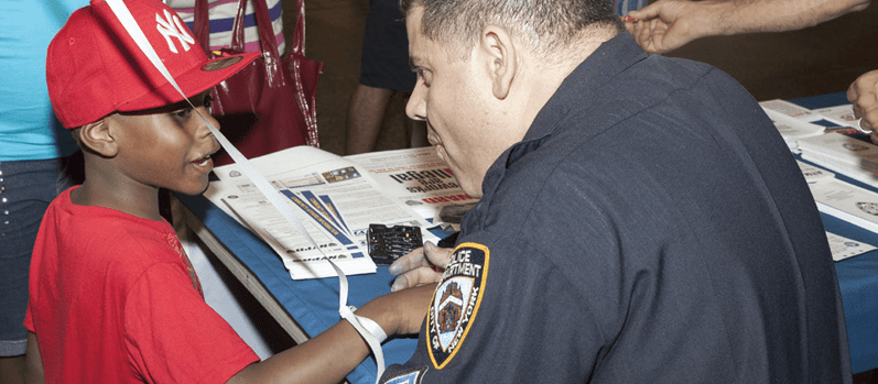 Two NY Police Department officers talk to commuters at a New York City subway station, one speaks to a young boy.