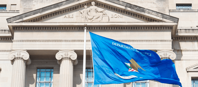 Department of Justice flag in front of the main Department of Justice building Blue Department of Justice flag waving in front of the main Department of Justice building.