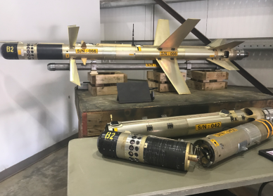 Two black and tan surface to air missiles that were part of the seizure. One is one display on top of a wooden box and the other is in parts on a different box.