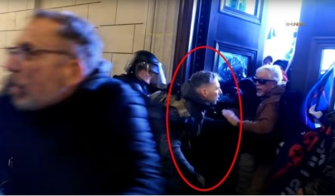 Warnagiris seen helping individuals through the east rotunda door as a USCP officer attempts to pull him away from the doorway. Camera footage screenshot