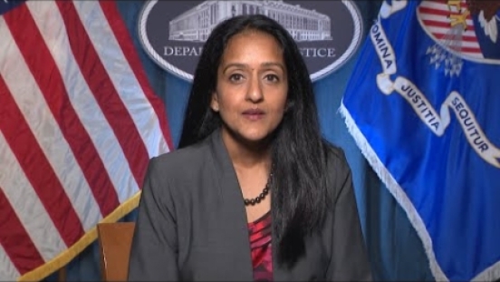 Associate Attorney General Gupta in front of US and DOJ flags