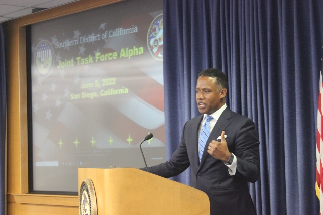Assistant Attorney General Kenneth A. Polite, Jr. giving a presentation with a slide titled Joint Task Force Alpha in the background