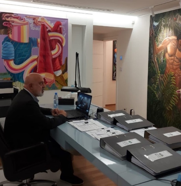 Chicago Art Gallery-1 Painting Hanging (on right) before Ahmad sitting at a desk. A person sitting at a desk with large binders and a computer on the surface and large paintings hanging on the wall in front of him.